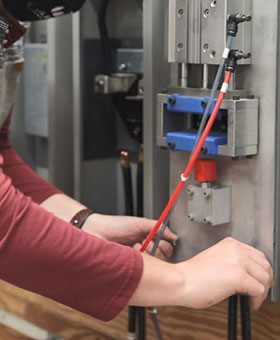 A pair of hands work with wires, testing a product in the Milbank engineering lab.